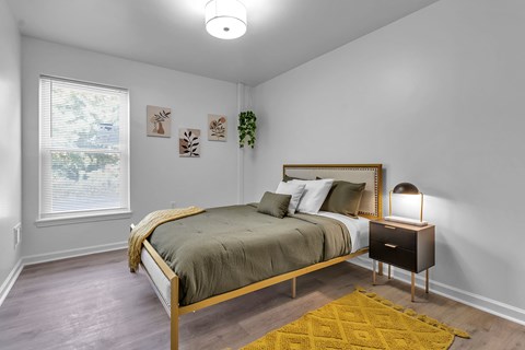 A bedroom with a bed, nightstand, and a window with blinds.