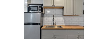 A kitchen with a stainless steel refrigerator, a microwave, and a sink with a wooden countertop.