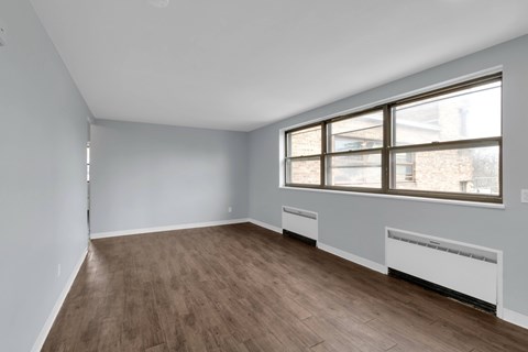 A room with wooden flooring and a window with a view of a building outside.