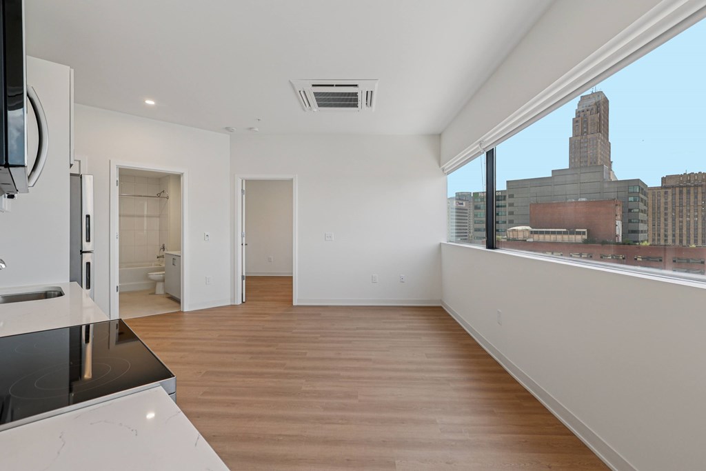A large empty room with wooden floors and a city view from the window.