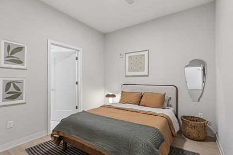 A bedroom with a bed, pillows, a basket, and a mirror. A bedroom with a bed, pillows, a basket, and a mirror at LiveWell Apartments, Pittsburgh 15222