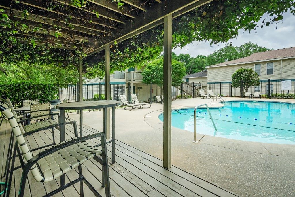 the pool is under a covered patio with chairs and a table