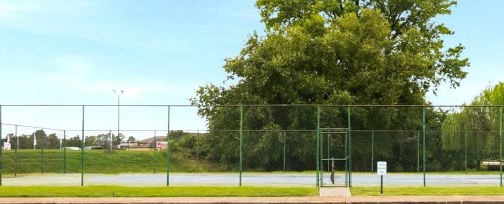 A green fence surrounds a tennis court.