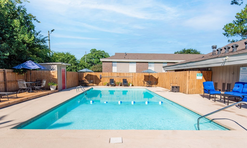 our resort style swimming pool is next to our house with chairs and a fence