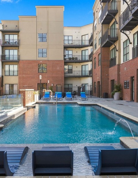 A pool surrounded by a brick building and lounge chairs.