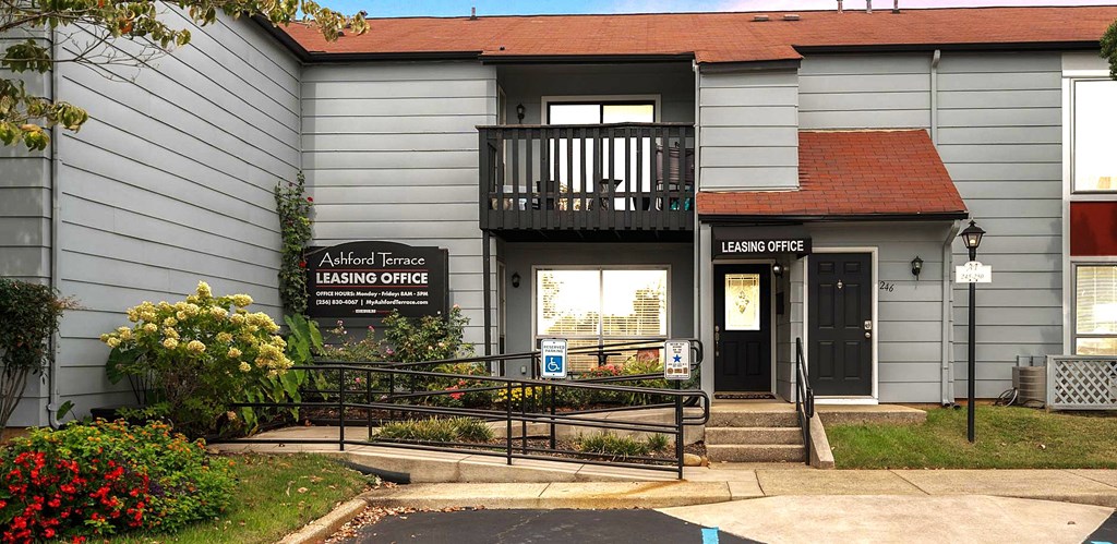 A grey building with a black sign that says Leasing Office.