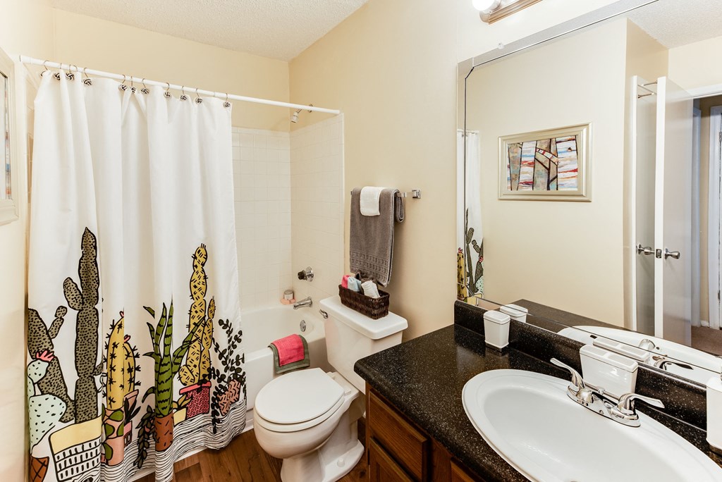 a bathroom with a white toilet next to a sink with a shower curtain with a cactus