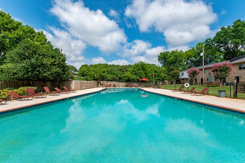 A large swimming pool surrounded by trees and lawn chairs.