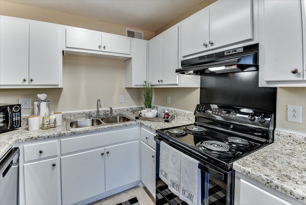 an all white kitchen with granite counter tops and a black stove and oven and sink