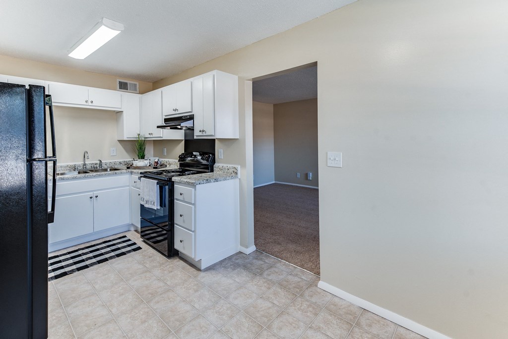 an empty kitchen with white cabinets and a black refrigerator