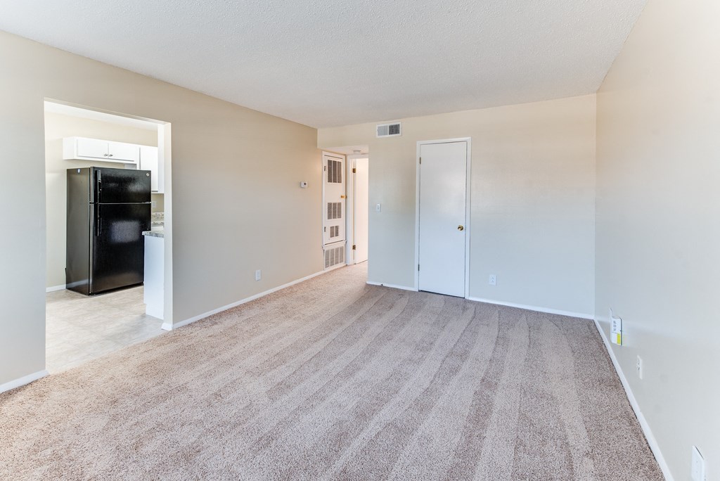 an empty living room with a kitchen and a refrigerator