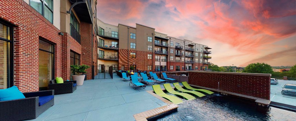 a pool with blue lounge chairs in front of an apartment building at sunset