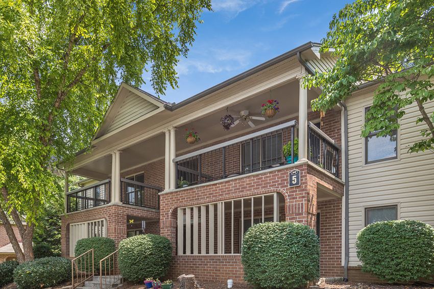 the view of the front of a brick house with a balcony and a tree