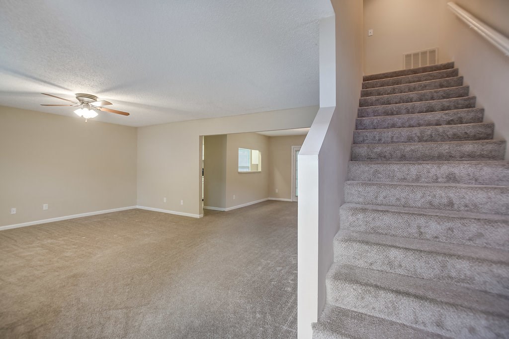 a carpeted living room with stairs and a ceiling fan