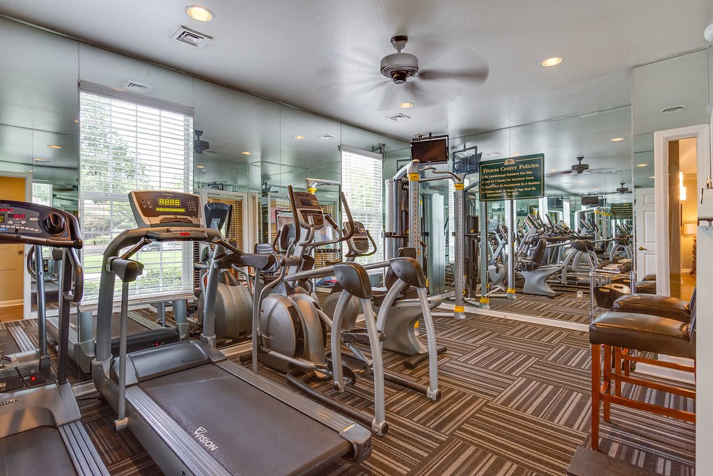 a gym with cardio machines and a ceiling fan