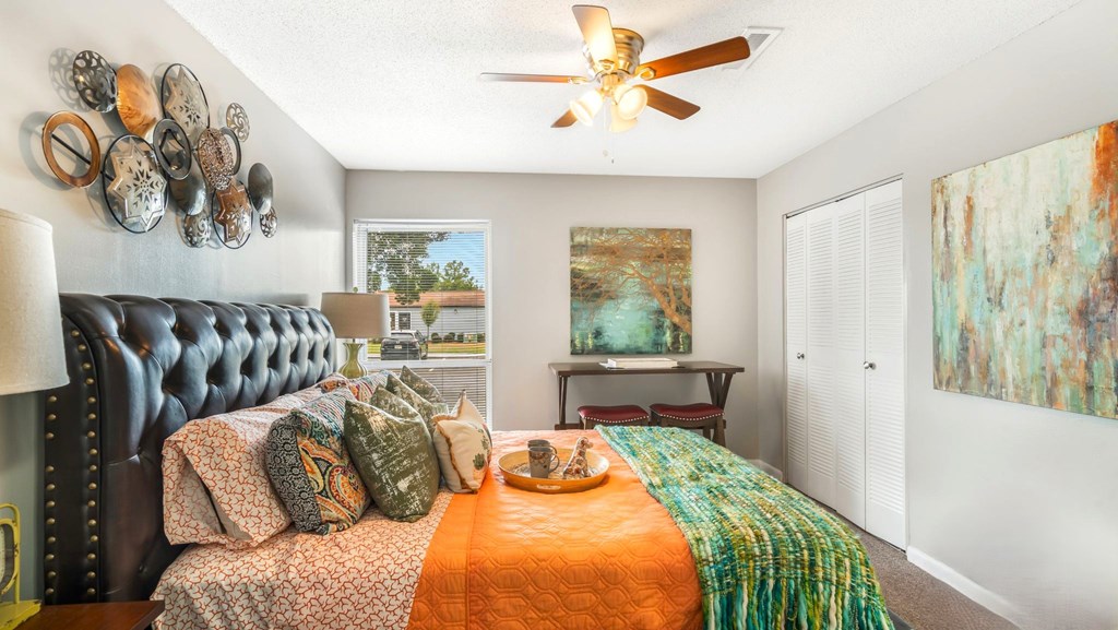 A bedroom with a black headboard and a bed with orange and green bedspread.