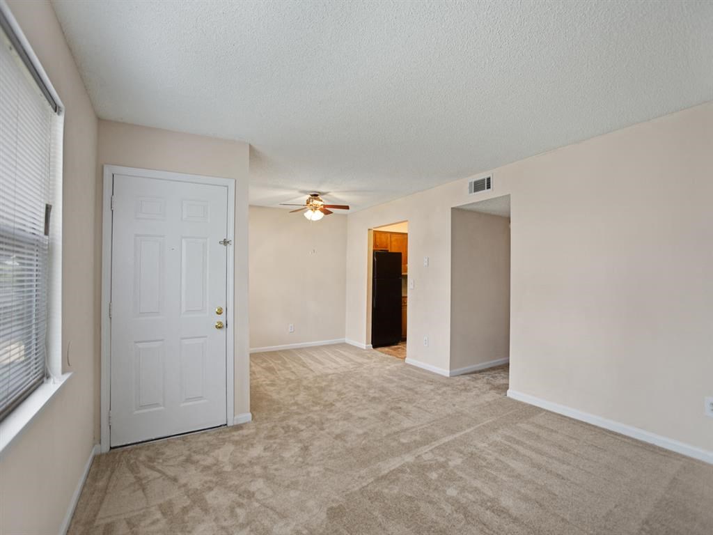 an empty living room with a white door and a ceiling fan