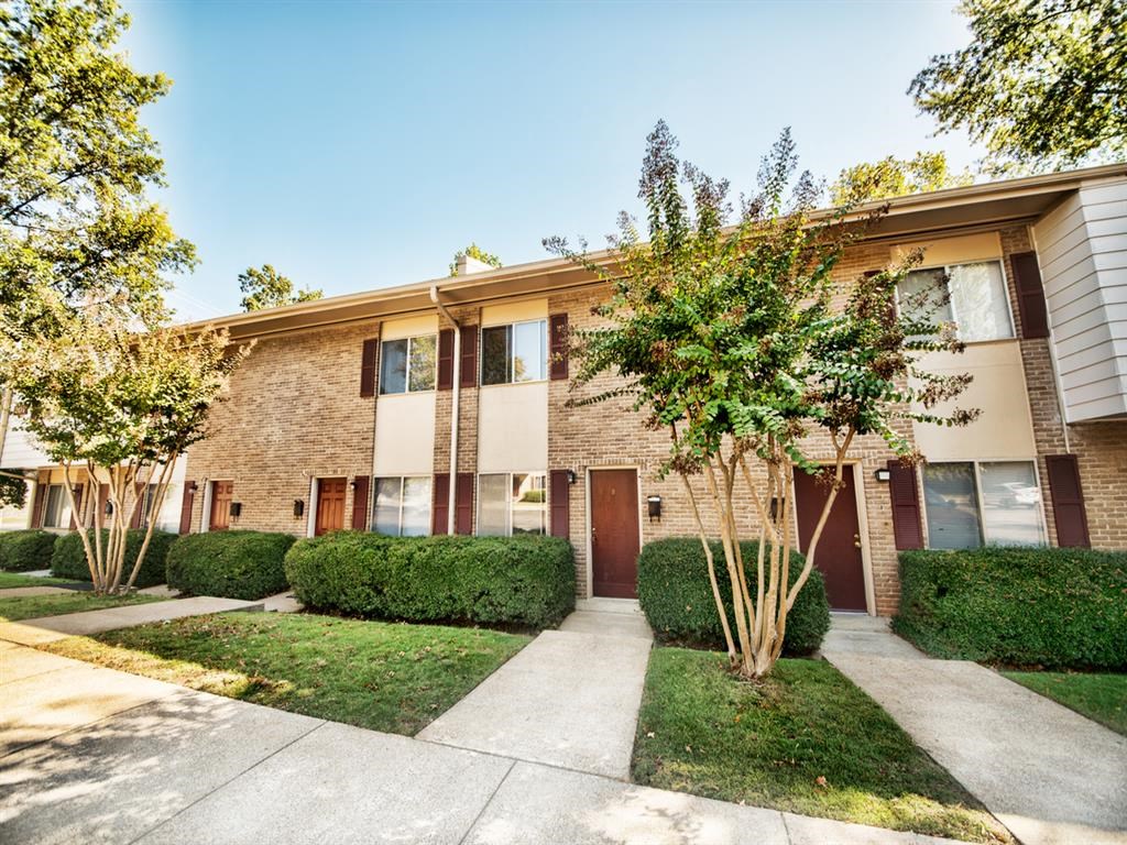 an apartment building with a sidewalk and trees in front of it