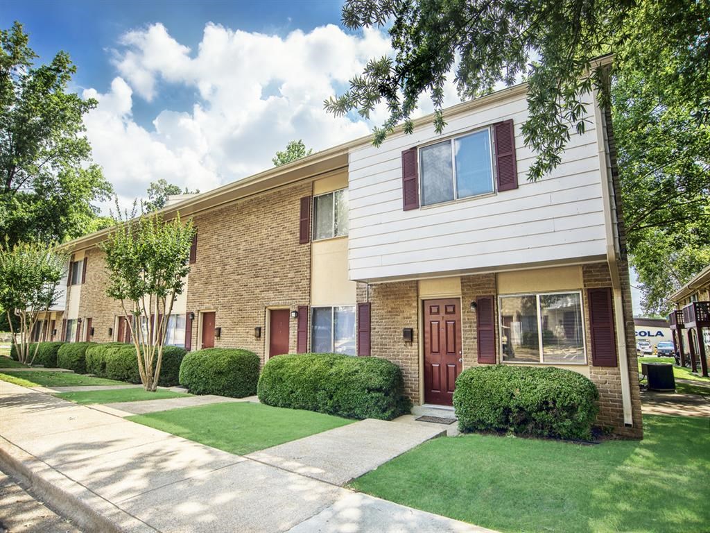 the front of a brick apartment building with a sidewalk and grass