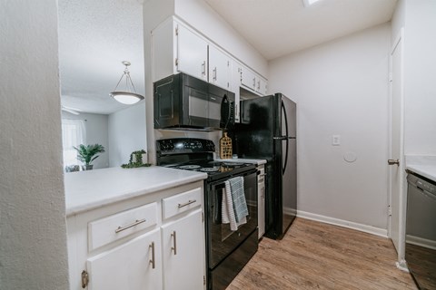 A black refrigerator stands in a kitchen with white cabinets and a white countertop.