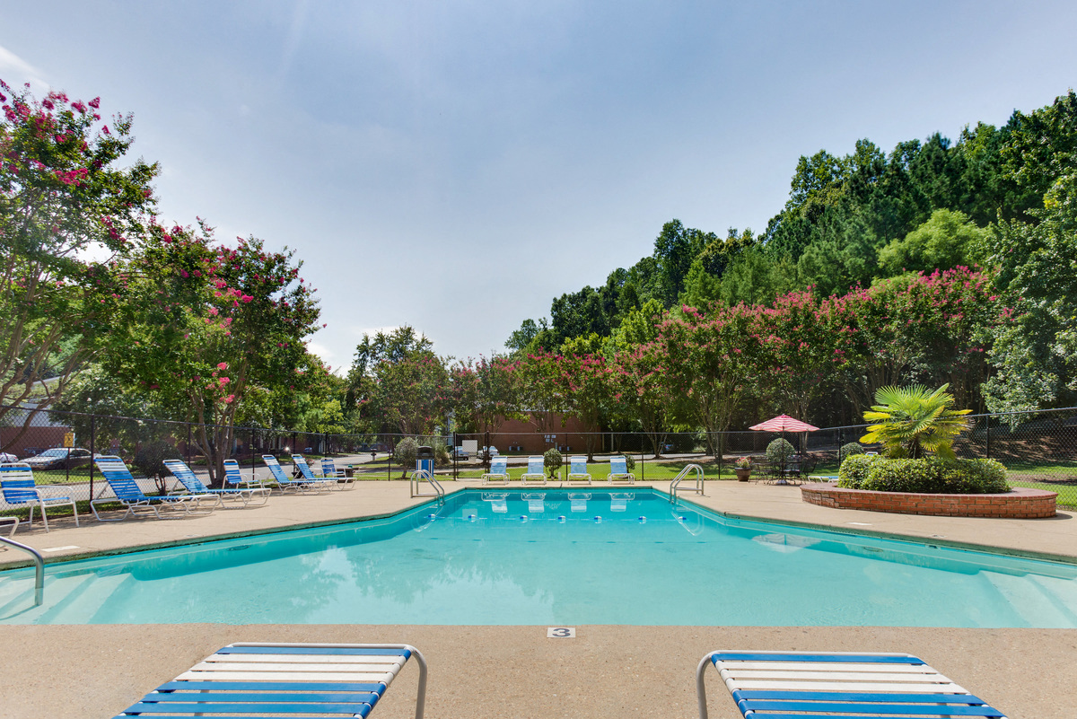 a swimming pool with chairs and trees in the background