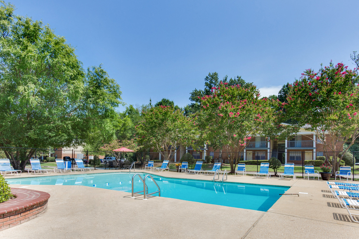 a swimming pool with chairs and trees and a building in the background