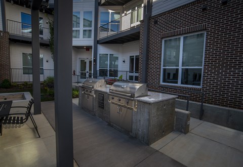 A BBQ grill is on a patio in front of a brick building.