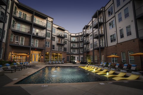 A swimming pool surrounded by yellow sun loungers in front of apartment buildings.