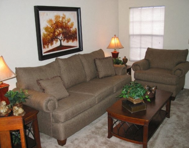 A living room with a brown couch, a brown armchair, a coffee table, and a framed picture of a tree.