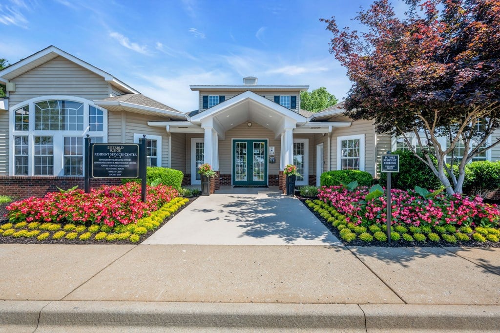 the front of a white house with flowers and a sign on the sidewalk