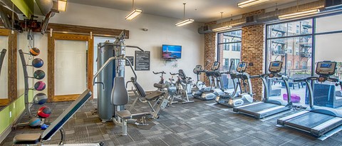 a gym with cardio machines and weights on a brick wall