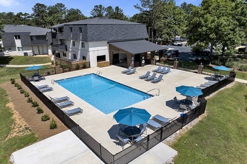 A large swimming pool surrounded by a black fence and blue umbrellas.