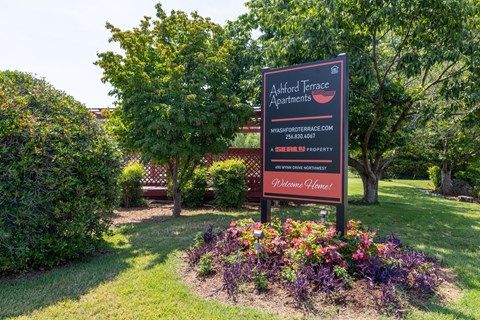 a sign in a park with flowers and trees