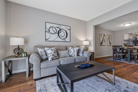 A modern living room with a grey couch, a coffee table, and a dining table set in the background.