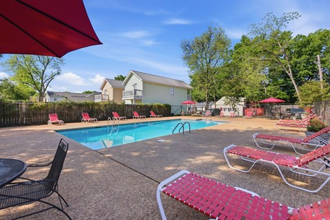 A pool area with red lounge chairs and umbrellas.