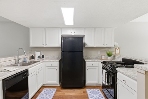A black refrigerator in a kitchen with white cabinets and a marble countertop.