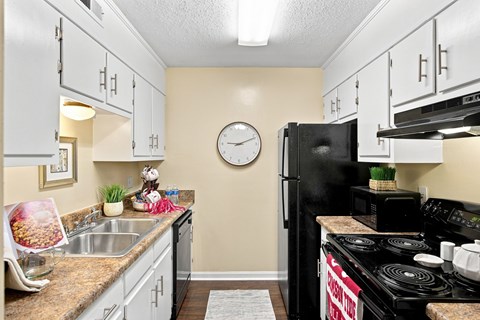A kitchen with a black refrigerator and a clock on the wall.