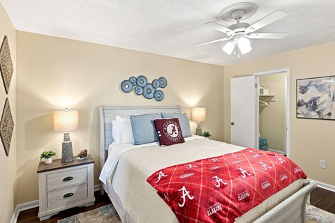 A bedroom with a bed covered in a red Alabama football bedspread.