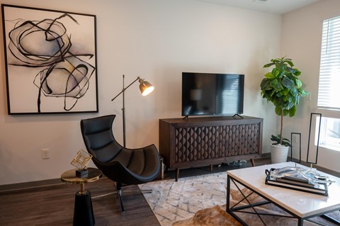 A black chair sits in a living room with a large abstract painting on the wall.
