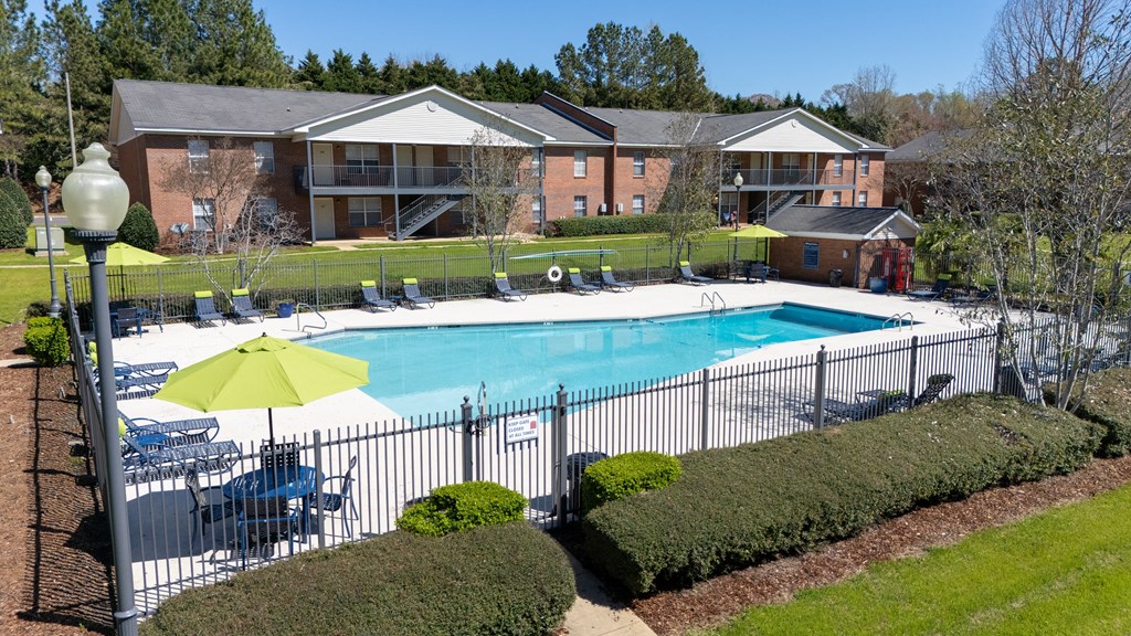 A pool surrounded by a fence and bushes with a building in the background.