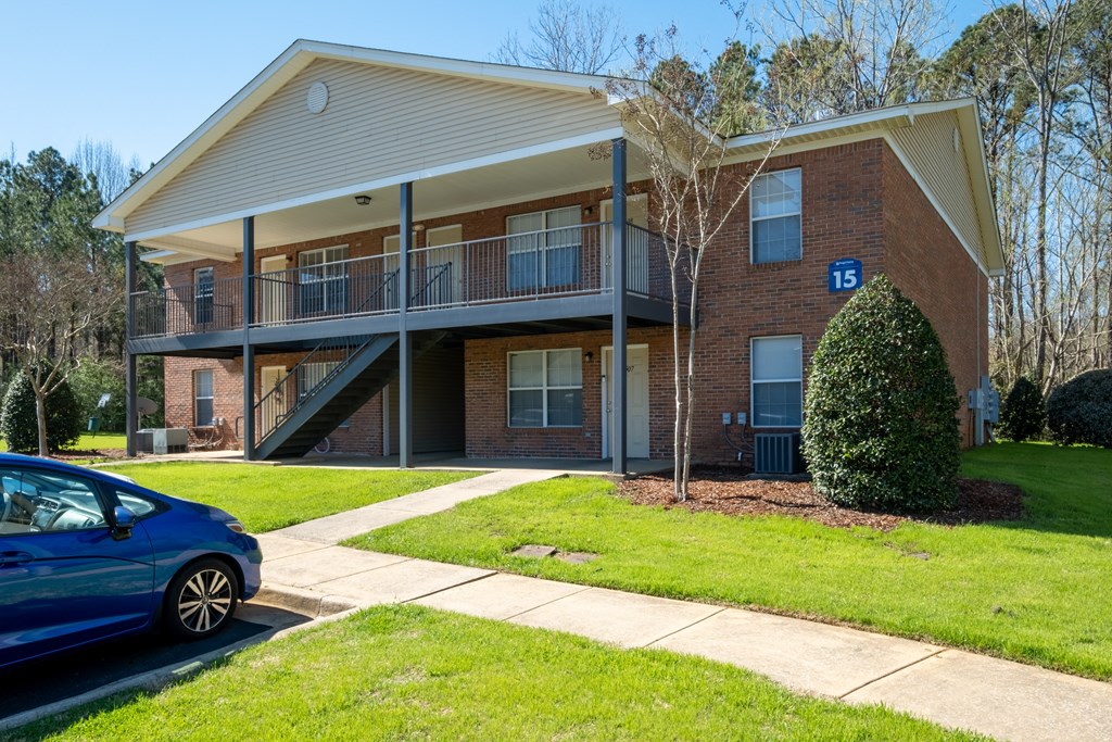 A blue car is parked in front of a two-story brick apartment building.
