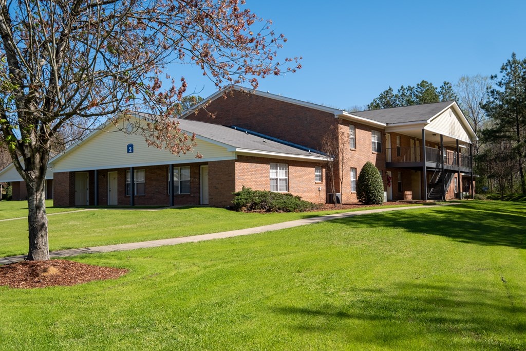 A tree with brown leaves stands in front of a building with a yellow roof.