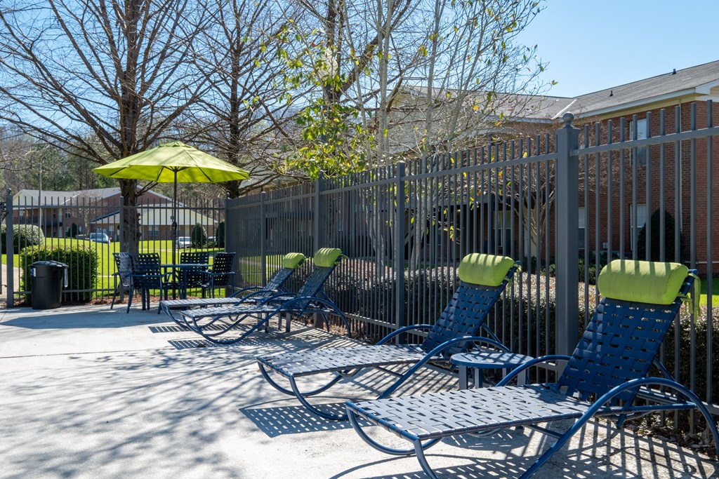 A row of blue lawn chairs with green cushions are lined up on a patio.