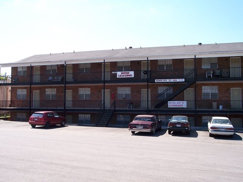 A red car is parked in front of a brick apartment building.