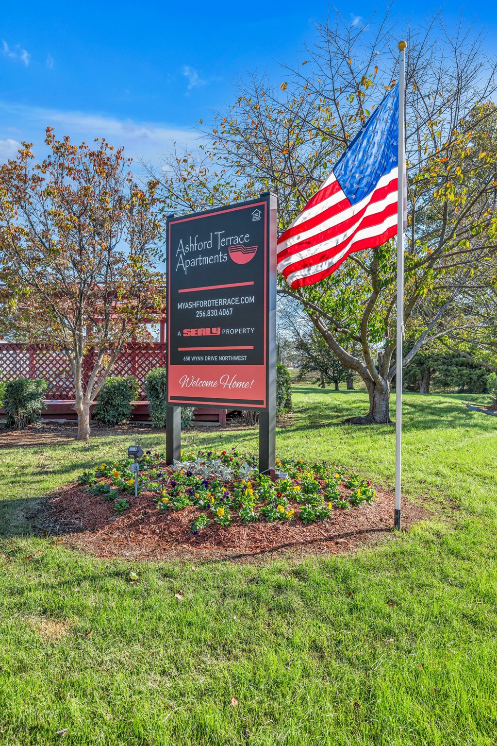 A sign for Ackford Terrace Apartments is in front of a tree and an American flag.