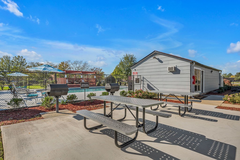 A picnic table is in the foreground of a sunny day with a pool and a building in the background.