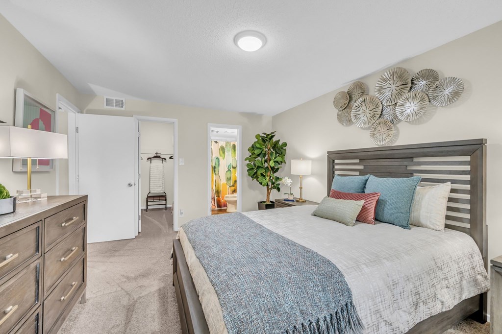 A bedroom with a bed, dresser, and a plant.