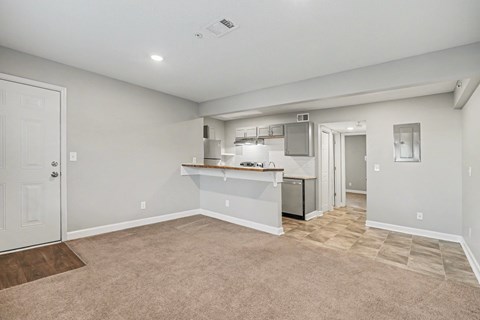 A spacious room with a kitchenette and a door leading to another room.