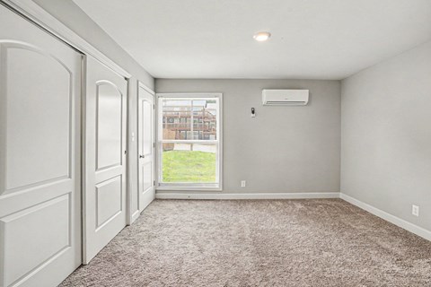 A room with a carpeted floor and a window showing a fence and a building outside.