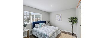 A bedroom with a bed, a plant, and a painting on the wall.